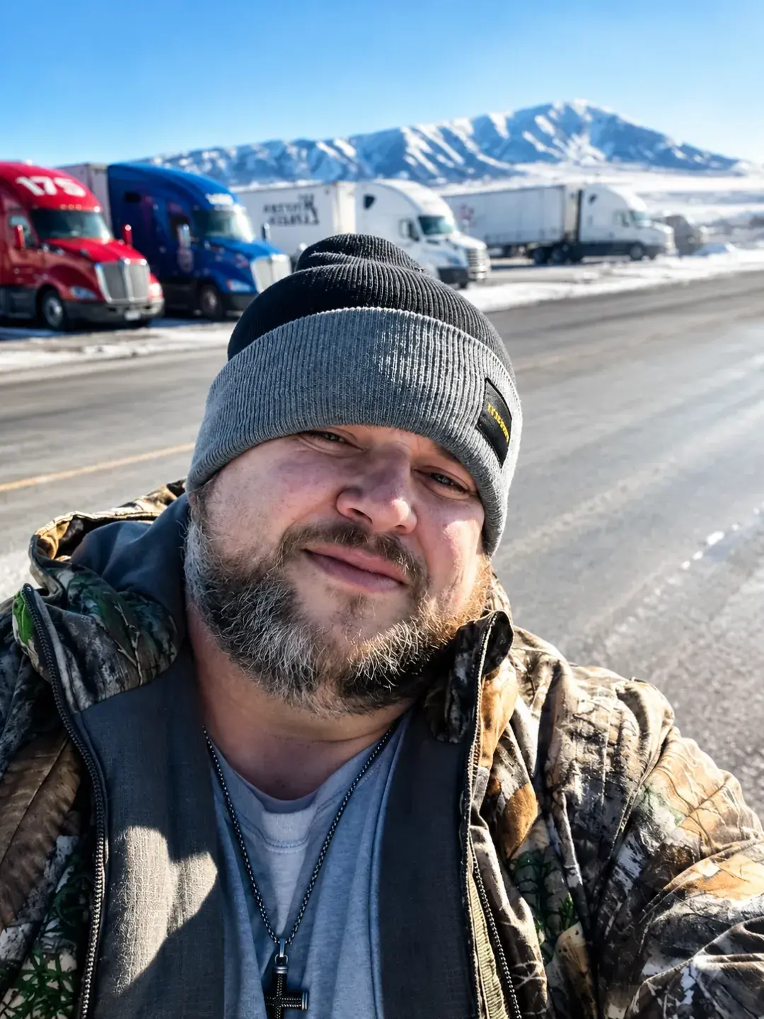 Shawn during his trucking years with tractor-trailers parked behind him in a snowy mountain setting.