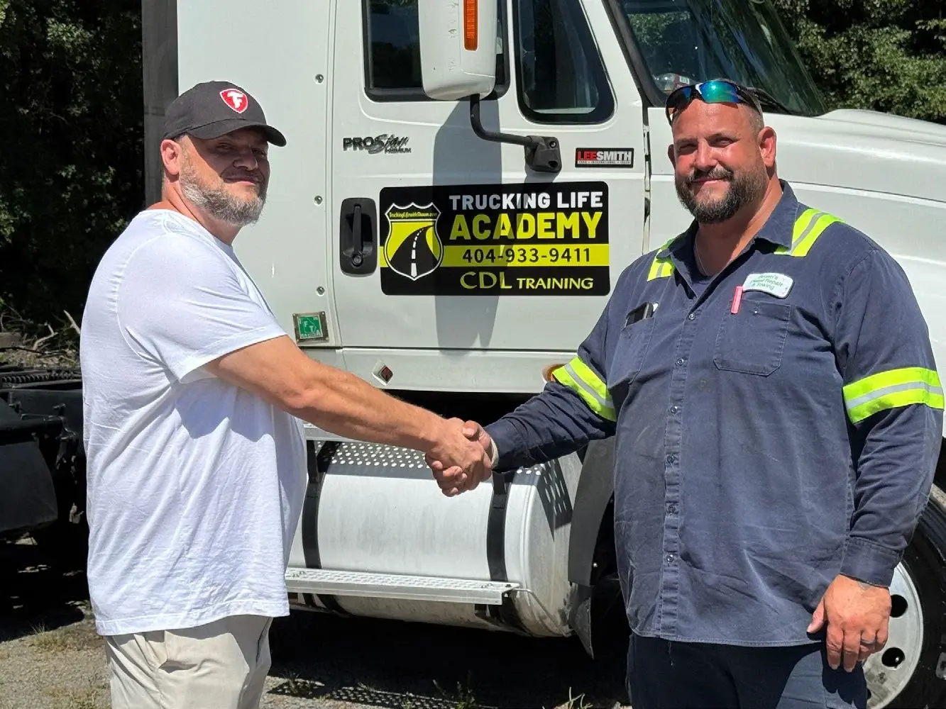 Two men shaking hands in front of a Trucking Life Academy training truck, as published with the Gordon Gazette story